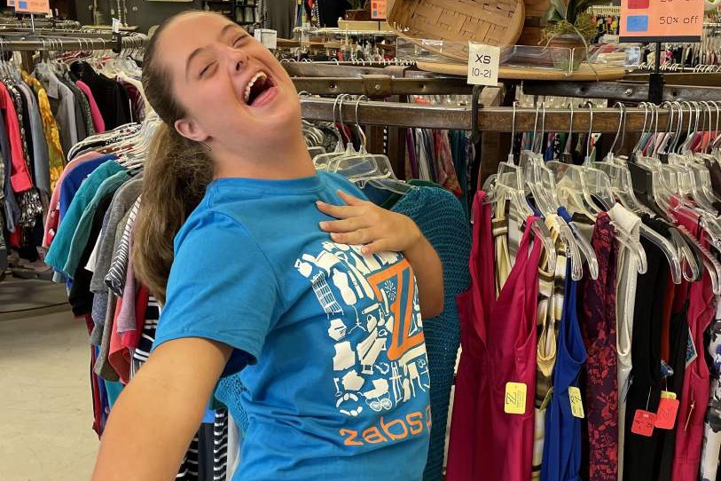 A young adult laughing while working among the clothing racks at ZABS Place